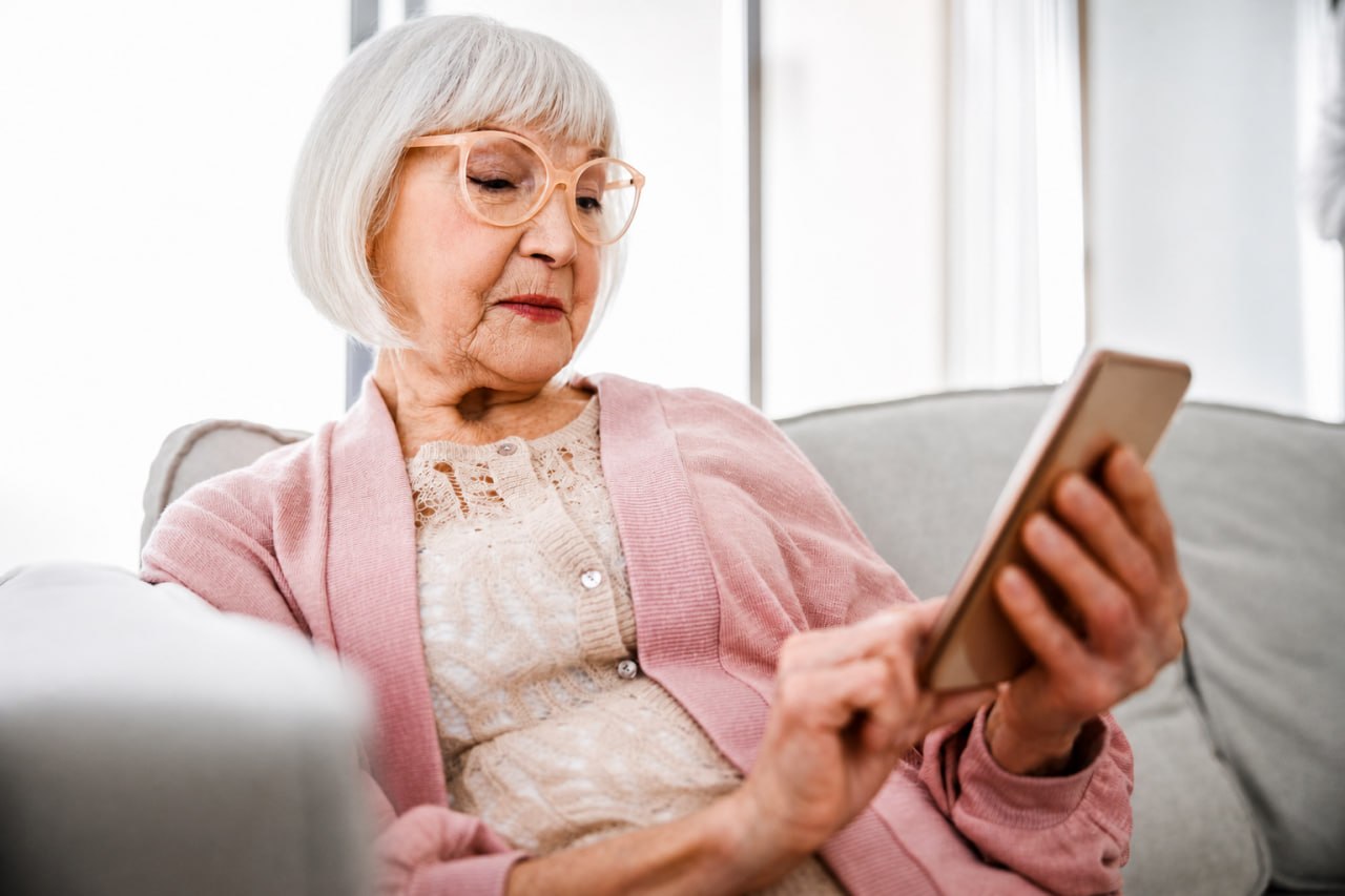 An older woman sitting at home and reading on her phone